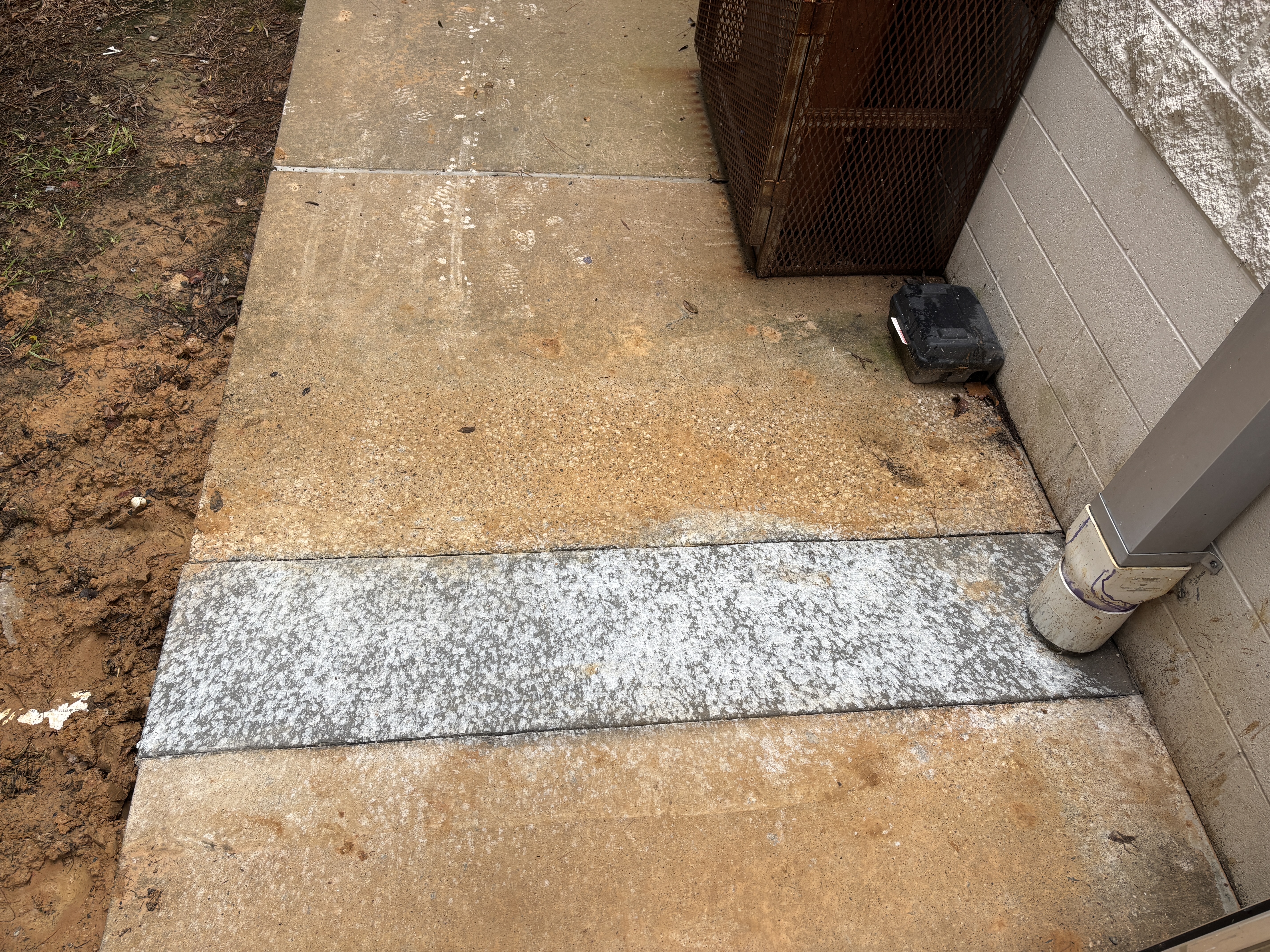 Downspout tied into a PVC boot at grade with a fresh saw-cut concrete patch running under the walkway to the storm line