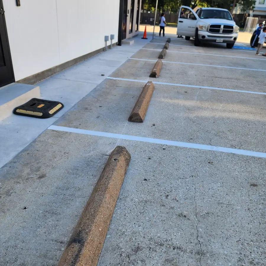 Precast concrete wheel stops set one per stall on a freshly striped commercial concrete parking lot alongside a storefront sidewalk